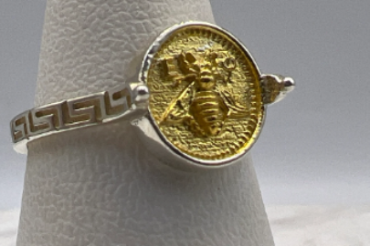 Gold ring with bee design on a gray stand